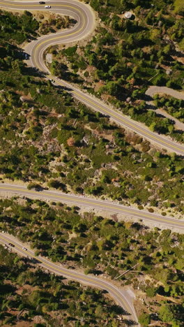 cars moving leisurely by the winding road going through the green landscape. drone descending over the highway on sunny daytime. vertical video