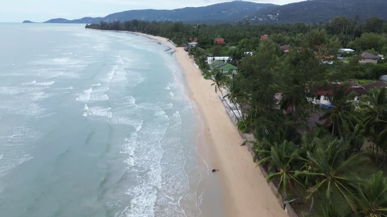 Aerial drone view of Lamai Beach in Koh Samui, Thailand, showing turquoise sea, sandy shoreline, palm trees, and tropical island landscape under bright sunlight