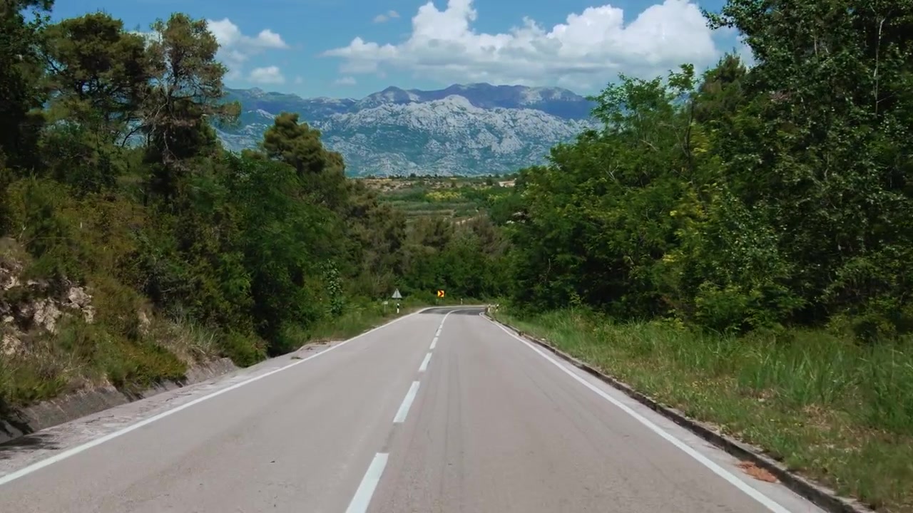 Guidando su una strada costiera panoramica vicino a Zara, di fronte alle lontane montagne del Velebit sotto un cielo soleggiato in Croazia