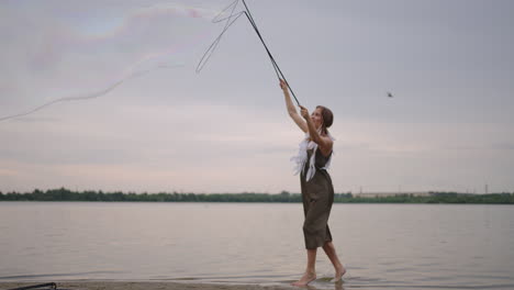 a young girl artist shows magic tricks using huge soap bubbles. create soap bubbles using sticks and rope at sunset to show a theatrical circus show