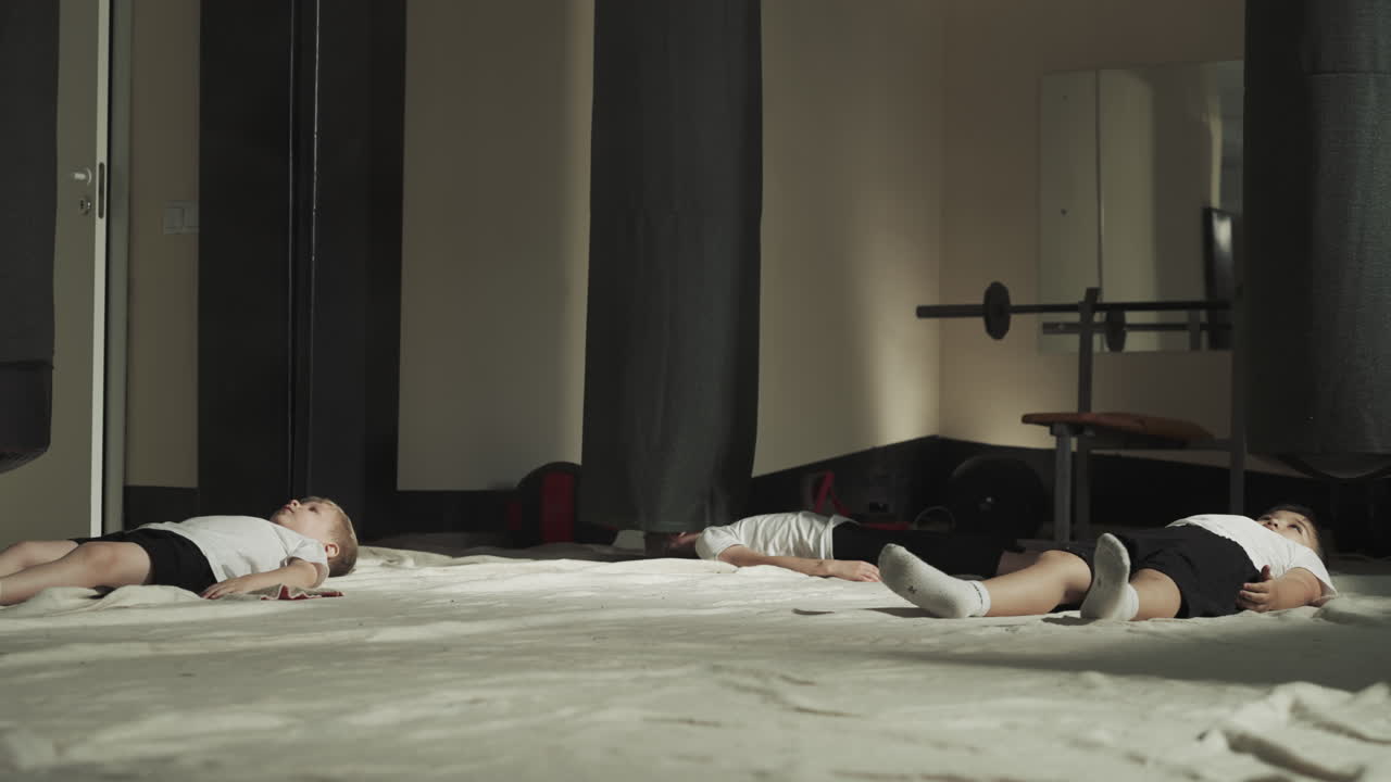 дети лежат на полу в спортивном центре после тренировки. маленькие ученики боевых искусств устали от упражнений кикбокса в боевом тренажерном зале в медленном движении.