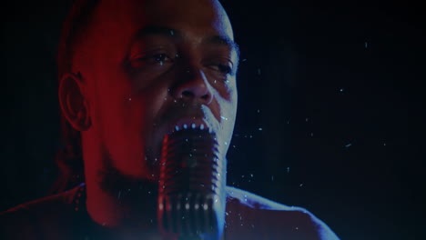 male singer performing on music stage, with retro microphone, red blue lights, floating drops