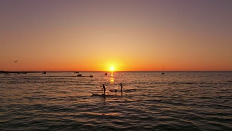 Toma-Aérea-De-Un-Par-De-Paddleboarding-Durante-La-Puesta-De-Sol-En-Iquique,-Chile