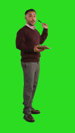 vertical video full length studio portrait of mature male teacher with notebook talking to class standing against green screen 3