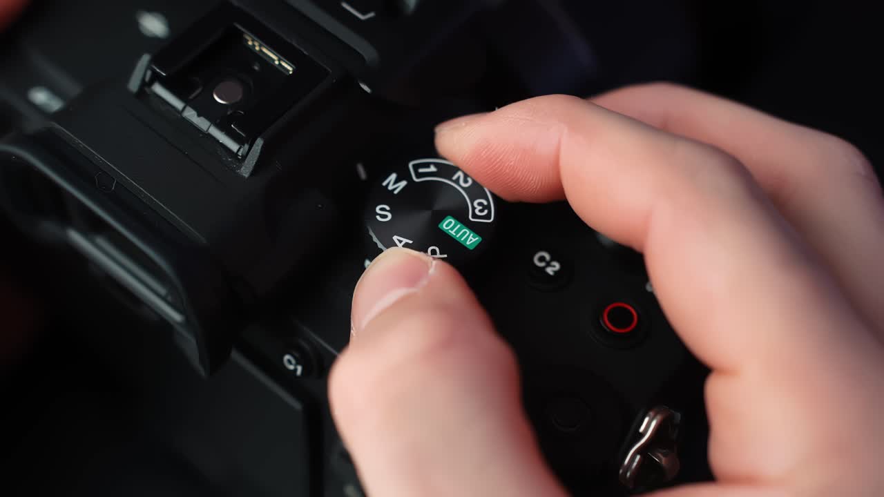 Nahaufnahme einer Hand, die das Moduswahlrad an einer spiegellosen Kamera dreht, Aufnahmemodi bei Studiolicht mit geringer Schärfentiefe für Creator Tech B-Roll wechselnd.