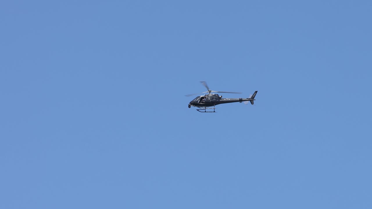 A helicopter progresses through a sunny, cloud-dotted sky