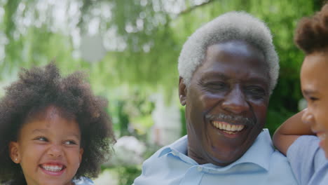 Loving-Grandfather-Talking-With-Grandchildren-In-Garden-At-Home