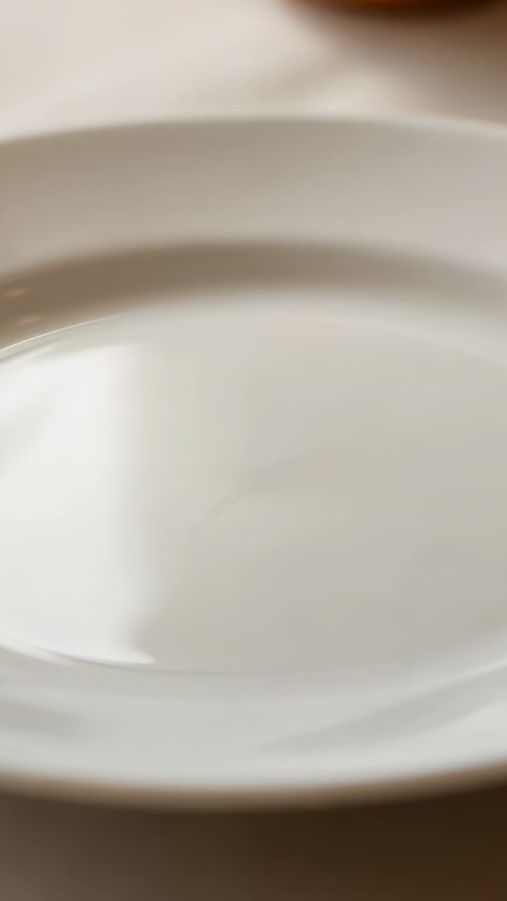 Vertical video: Camera shifting to reveal white plate on tablecloth, exposing glass and brown bun