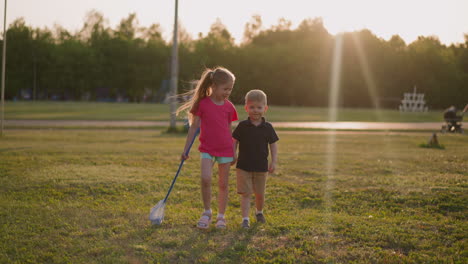 sister and little brother walk along playground at sunset