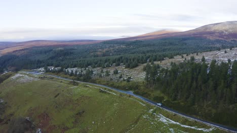 Viaje-Por-Wicklow:-Seguimiento-Aéreo-De-Un-Coche-Gris-Entre-Montañas-Brumosas-Y-Bosques-Cubiertos-De-Nieve