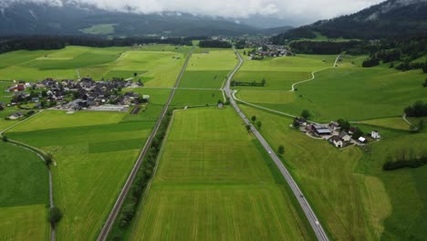 alpine serenity: 4k aerial drone shot of foggy drive from graz to hallstatt, cars wind through austrian countryside with perfectly mowed green fields and breathtaking alps panorama