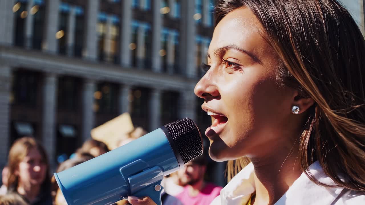 Wide-angle video shot of a diverse crowd at a women's rights protest, with a focus on a speaker