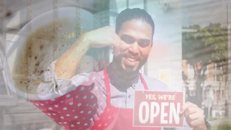 acercamiento de una taza de café contra un camarero afroamericano que sostiene un cartel abierto fuera del café