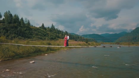 Couple-stands-on-bridge-over-a-mountain-river.-Love-of-man-and-a-woman