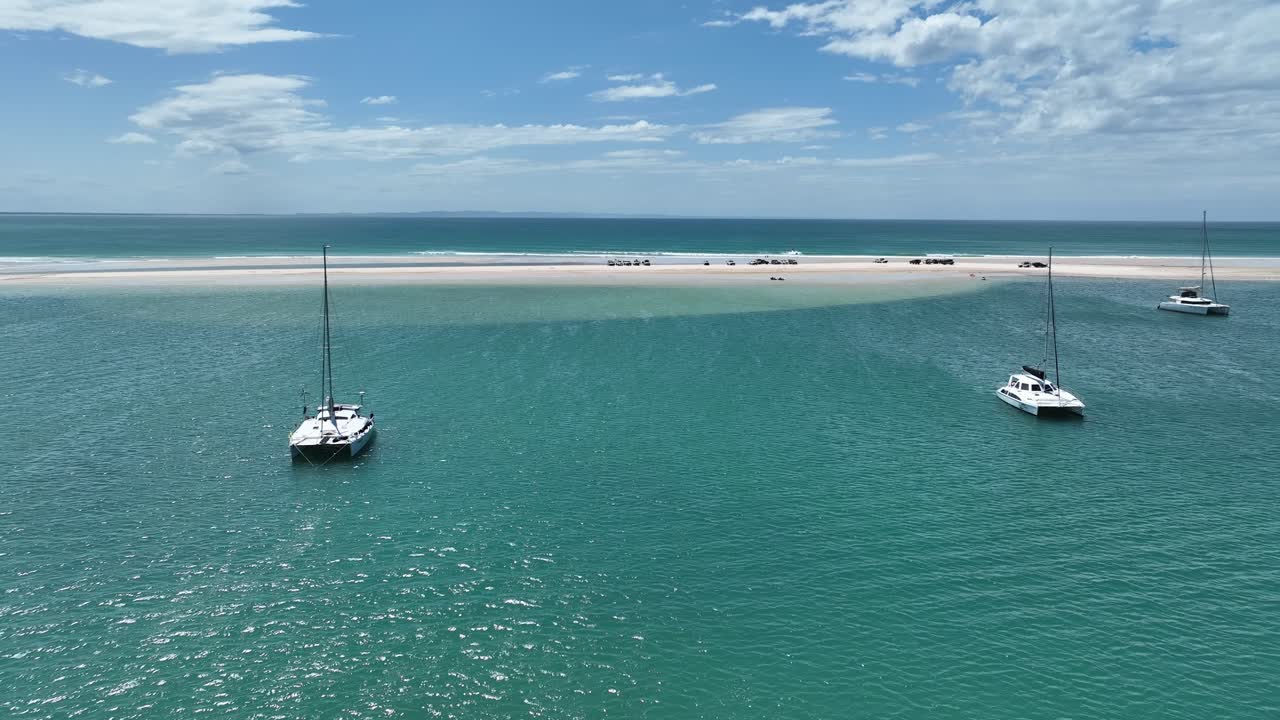 volando sobre el agua entre catamaranes hacia vehículos estacionados en un banco de arena