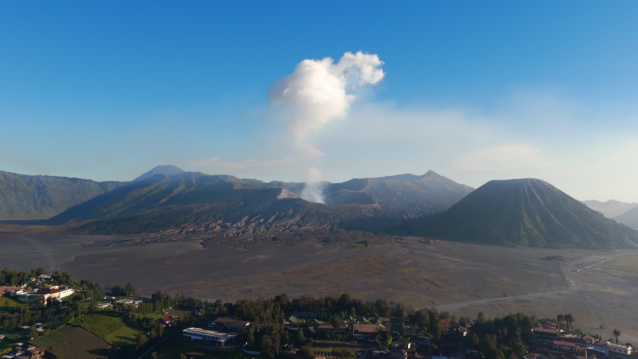 Pemandangan udara Desa Cemoro Lawang dengan Gunung Bromo dan Gunung Semeru di latar belakang, rekaman bergerak panoramik dengan kepulan asap