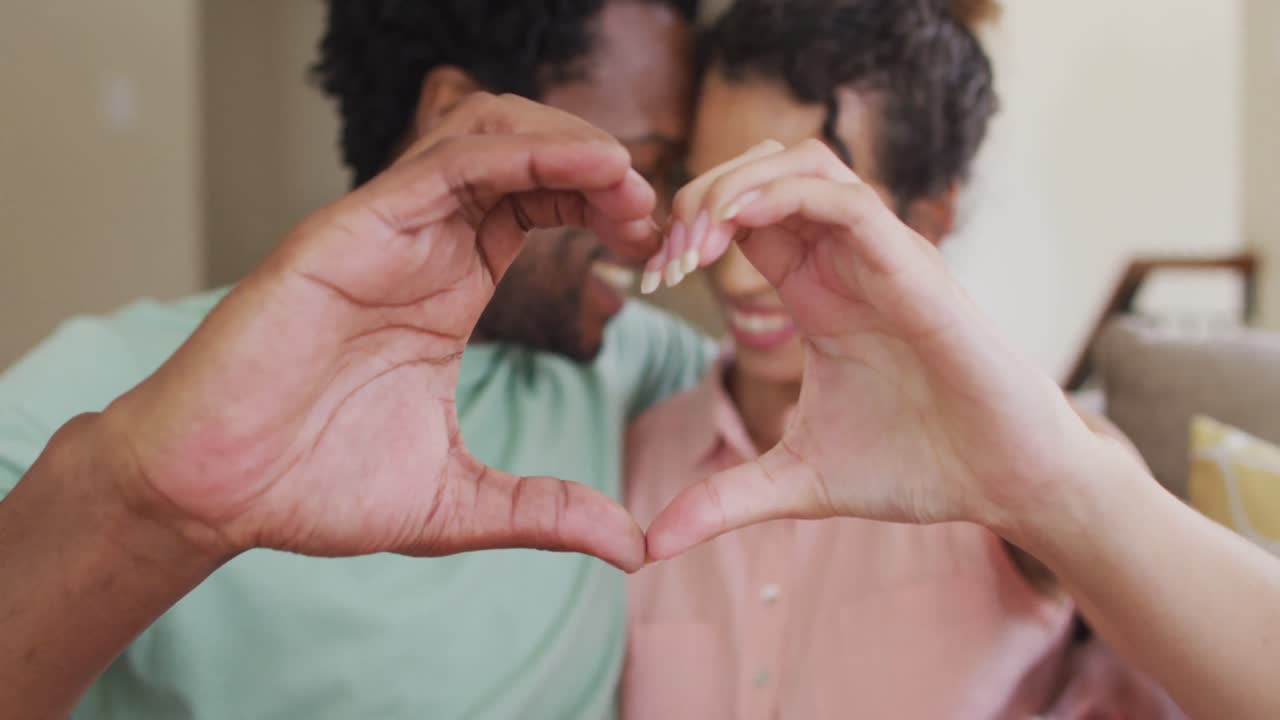 feliz pareja biracial haciendo gestos de corazón con las manos
