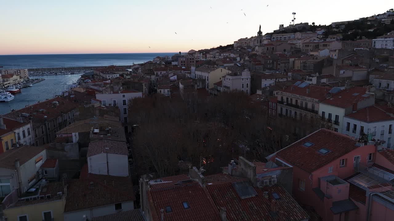 взгляд с дрона на приморскую деревню в конце дня при закате солнца, кадр сосредоточен вокруг площади с рождественскими украшениями.