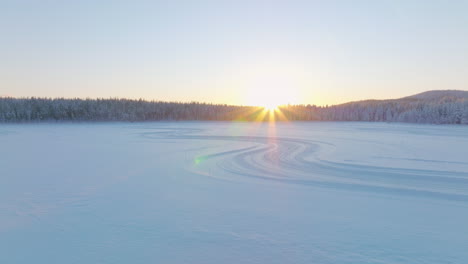 curving tyre tracks on norbotten polar circle ice lake rising aerial view to glowing sunrise skyline