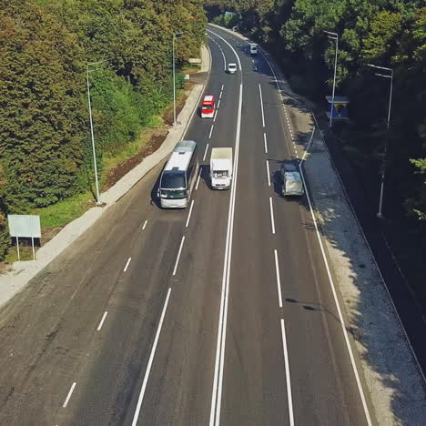 new road with four lines and the cars going by in summer. green trees growing on roadside of a two-lane road. bus stop from the right side of the road. aerial view along the highway