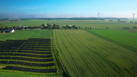 aerial view of agricultural green fields with solar farm and wind turbines in background