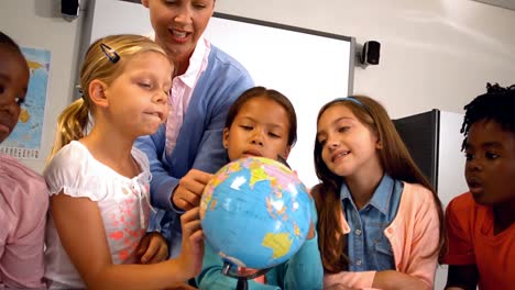 teacher discussing over a globe with kids in classroom
