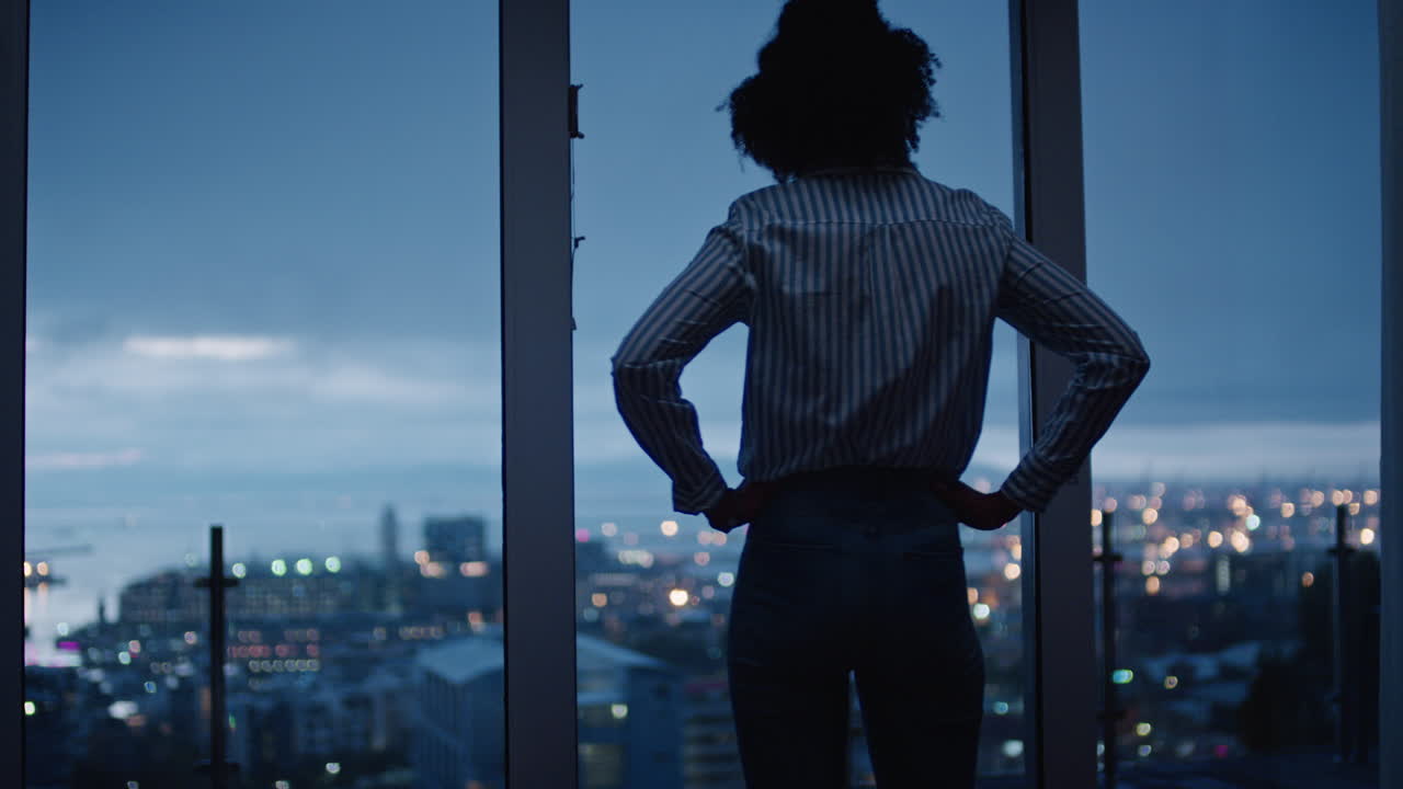 mujer joven mirando por la ventana disfrutando de la vista de la ciudad por la noche contemplando la planificación de un estilo de vida exitoso por delante en una tranquila noche urbana