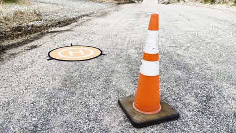 toma estática de una plataforma de aterrizaje de drones naranja y un cono de tráfico naranja en medio de una carretera pavimentada