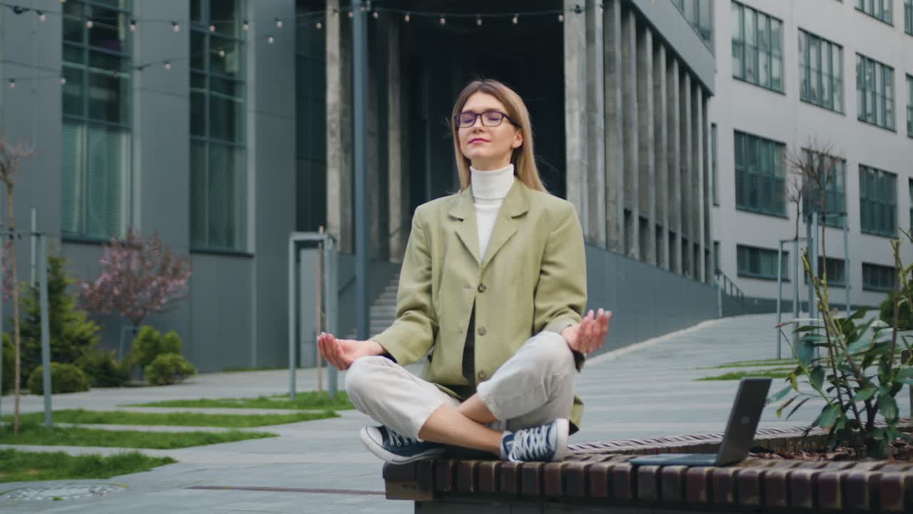Attractive businesswoman relaxing and meditating near modern office building. Beautiful girl doing yoga after a hard day's work