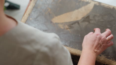 partial view of woman sketching shapes on dusty box using wet finger, capturing creative tactile moment during festive cozy indoor atmosphere, surrounded by rustic textures and soft natural light