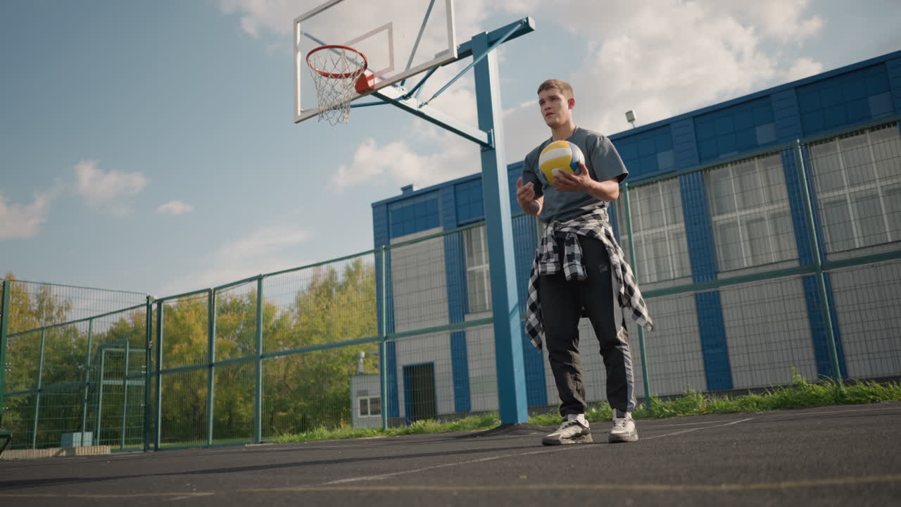 jugador de voleibol durante una sesión de entrenamiento rebotando el voleibol, girándolo en la mano antes de servir, capturado al aire libre en una arena deportiva con vegetación y edificio en el fondo