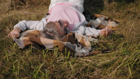 woman taking a photo with smartphone of a friend lying on hay with legs raised in air, sunny outdoor setting in a countryside field, capturing a fun and relaxed moment in nature