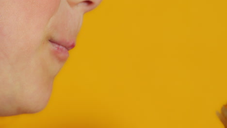 a close-up side view shows a child taking a big bite out of a pink frosted donut with colorful sprinkles, capturing the moment of enjoyment against a vibrant yellow background.