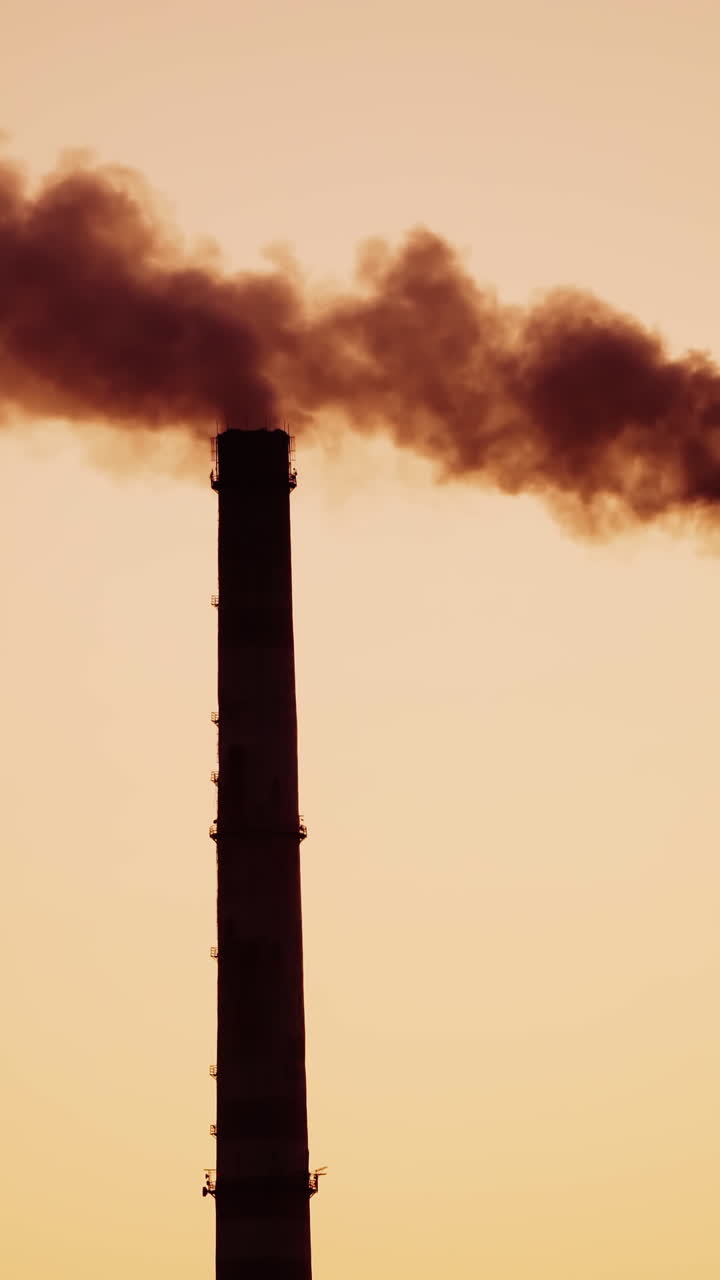 Industrial pipes with dark smoke at sunset. Dirty chemical smoke coming out from two pipes in the evening. Air pollution. Close-up. Vertical video