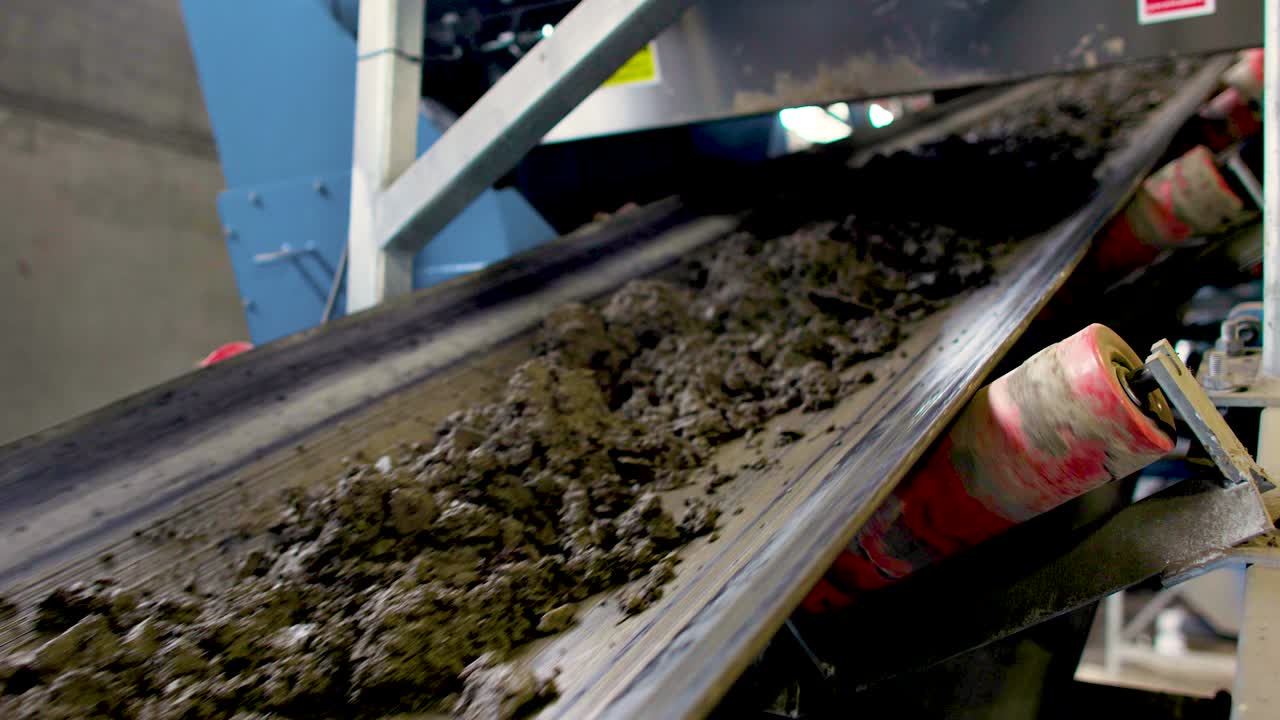 Static shot of dirt and rocks moving up a long conveyor belt with rollers moving.