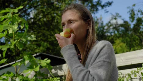 Girl-takes-bite-from-apple-and-stares-out-on-windy-day,-low-angle