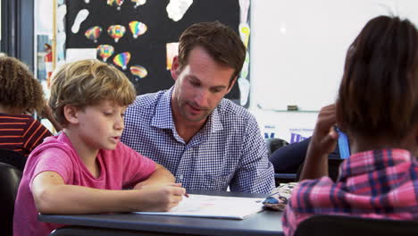 Teacher-and-young-schoolboy-looking-at-notebook-in-class