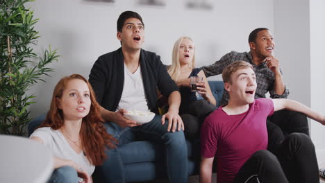 group of college friends celebrating whilst watching sports game on tv in shared house