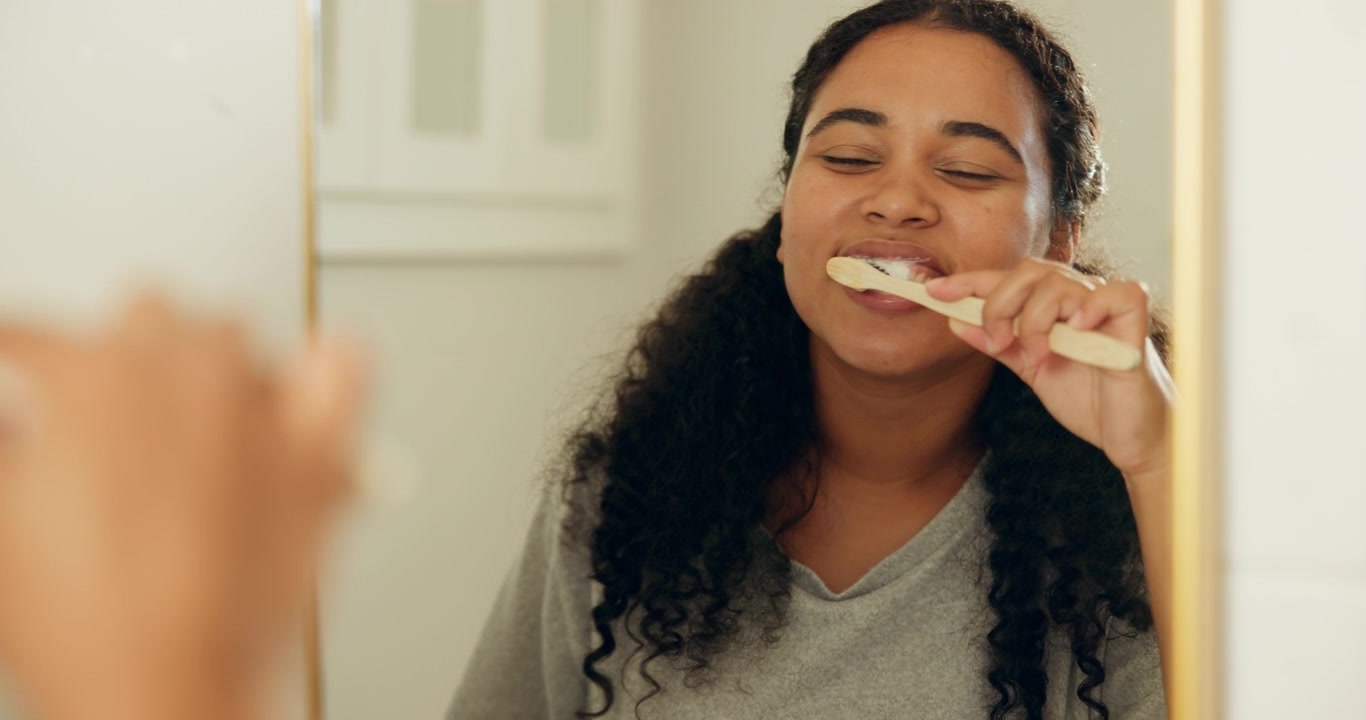 Young Woman Brushing Teeth in Bathroom Mirror