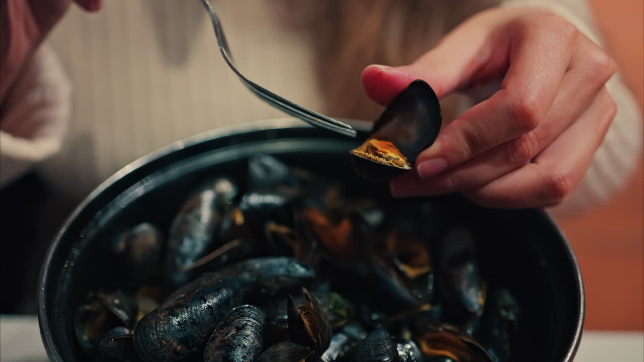 Close up of a woman eating mussels from a pan with a fork