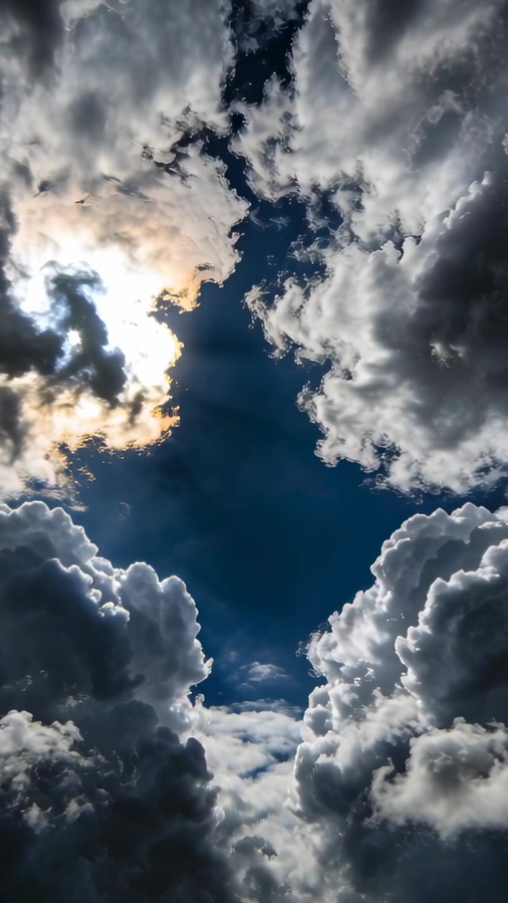 Vertical video: Shifting cumulus clouds streaming wisps into sky gap, sun hiding behind left cloud