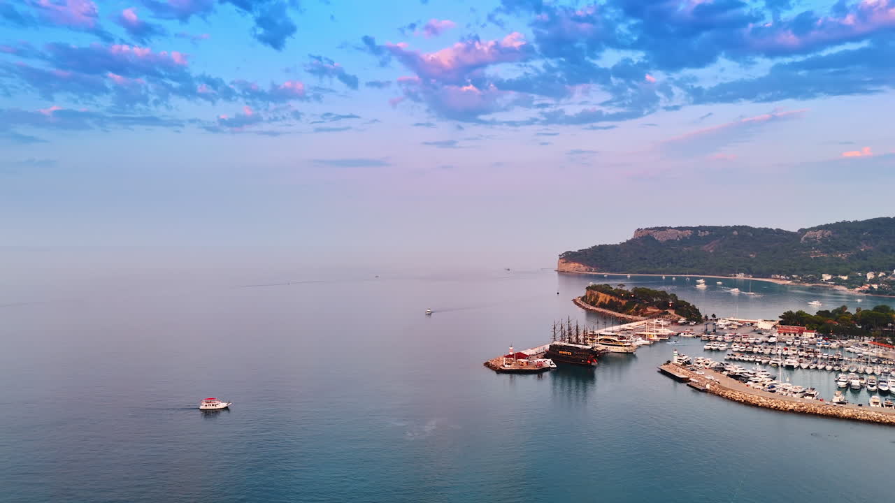 Rising over the pink waterscape merging with the sky at sunset. Ships and multiple yachts are at berth. Mediterranean of Turkey