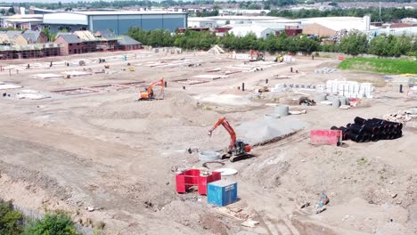 UK-town-housing-development-working-foundation-construction-site-digging-machinery-aerial-view-rising-tilt-down