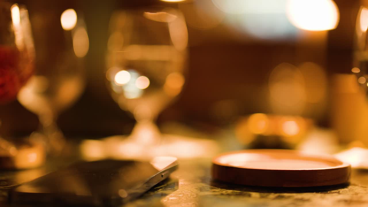 A hand lifts a cocktail glass from a bar counter under warm amber evening light