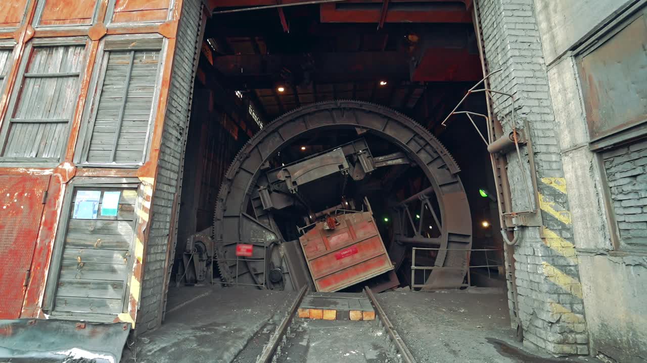 Device for unloading coal from wagon with a deaf body is rotating in the room of factory. Wagon tipper. Camera motion to back. Close-up.