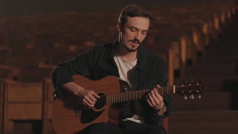 a handsome guy plays an acoustic guitar in an abandoned cinema. the musician sings a song and accompanies on the guitar