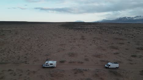 Two-white-camper-trucks-traverse-the-desolate-landscapes-south-of-Salt-Lake-City,-Utah,-USA,-aerial-perspective