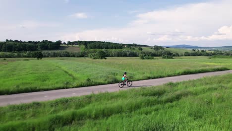 aerial tracking of young woman ride bike on countryside road in a green landscape, romania