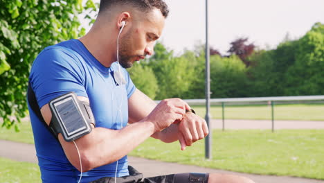 el hombre en la pista se pone los auriculares, establece la aplicación de reloj, comienza a correr