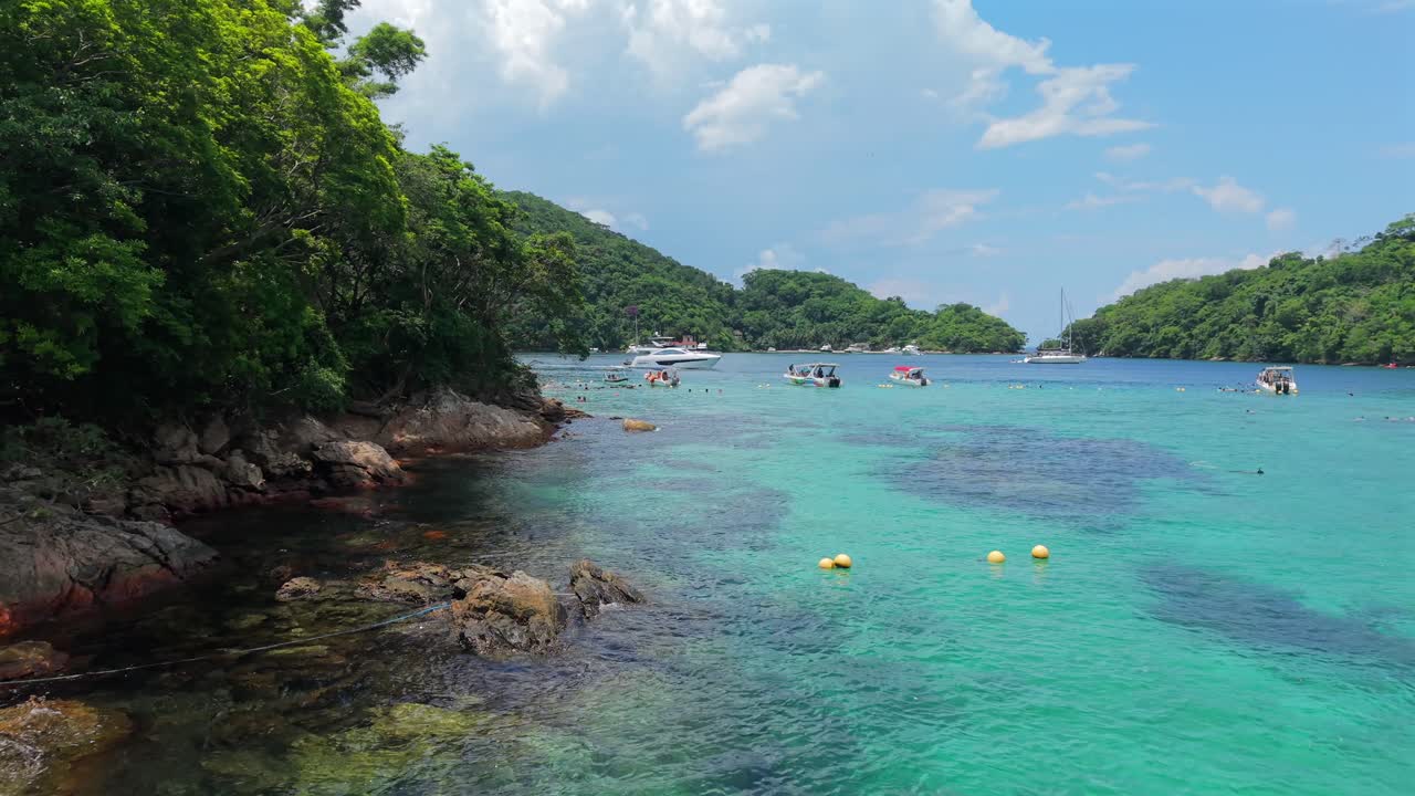 Acqua turchese limpida e barche ancorate a Lagoa Azul Ilha Grande Brasile, carrellata bassa verso l'area per snorkeling e nautica, ripresa con drone
